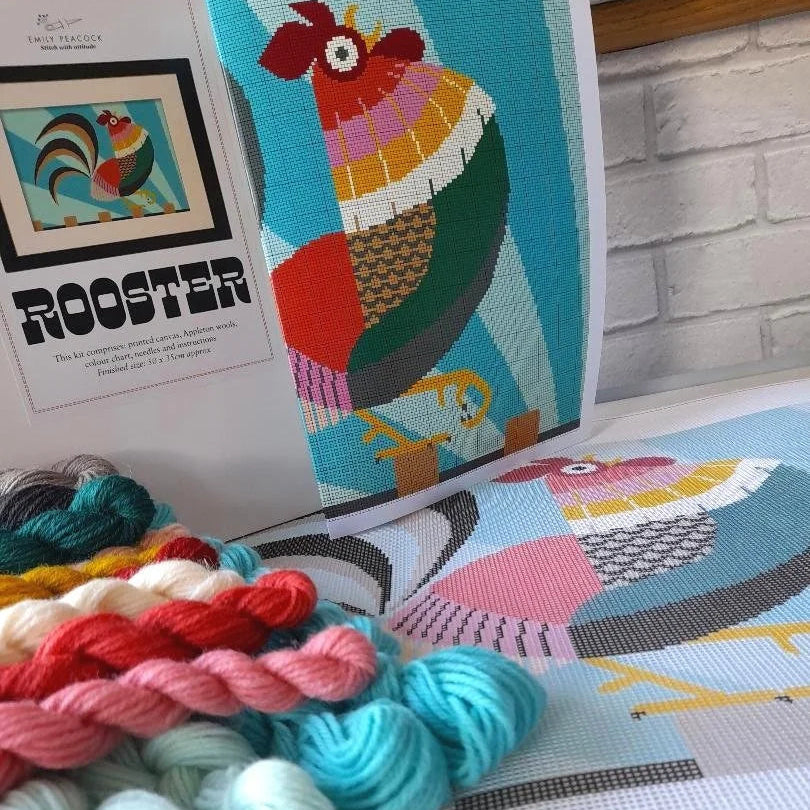 Colourful yarn skeins with cross stitch canvas and rooster design in the background