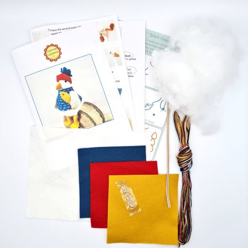 Contents of the folk embroidered seagull felt craft kit, including packaging, felt pieces, embroidery floss, ribbon, toy filling, needle, and instruction booklet