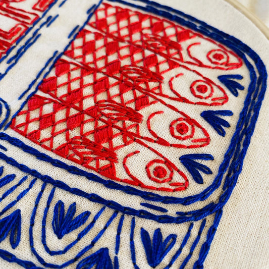 Close-up of an embroidery featuring canned red and blue sardines