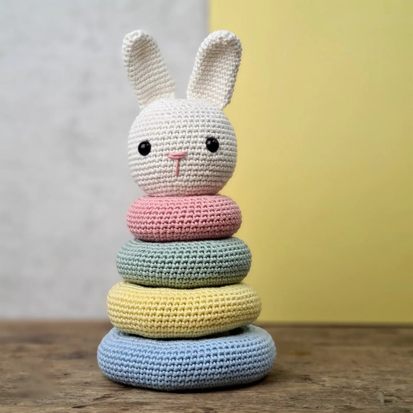 Crocheted bunny-shaped stacking toy with pastel colours on a wooden surface