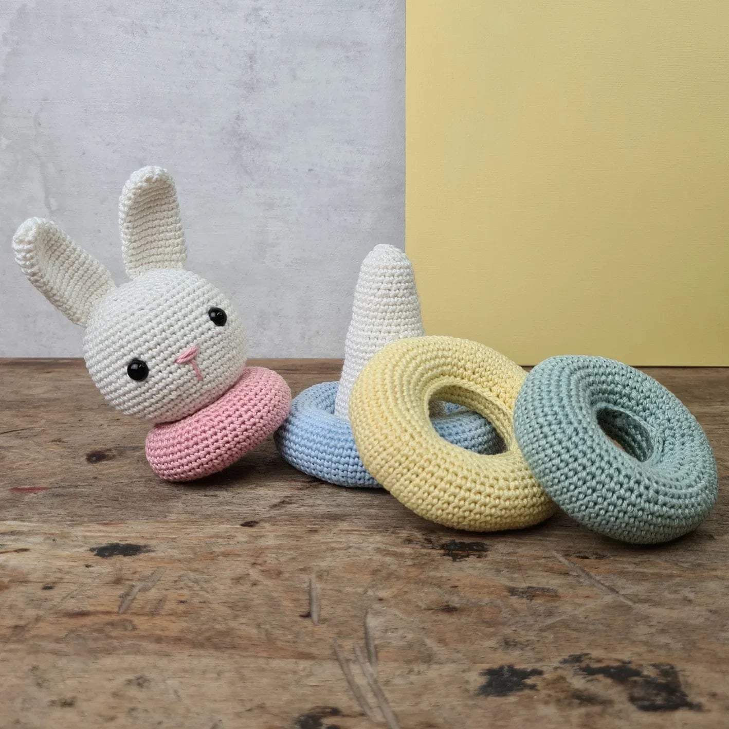 Crocheted stacking rabbit toy shown unassembled, with colourful rings on a wooden surface