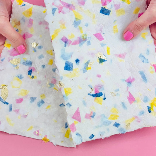 A person holding a completed piece of terrazzo-patterned paper on a pink background
