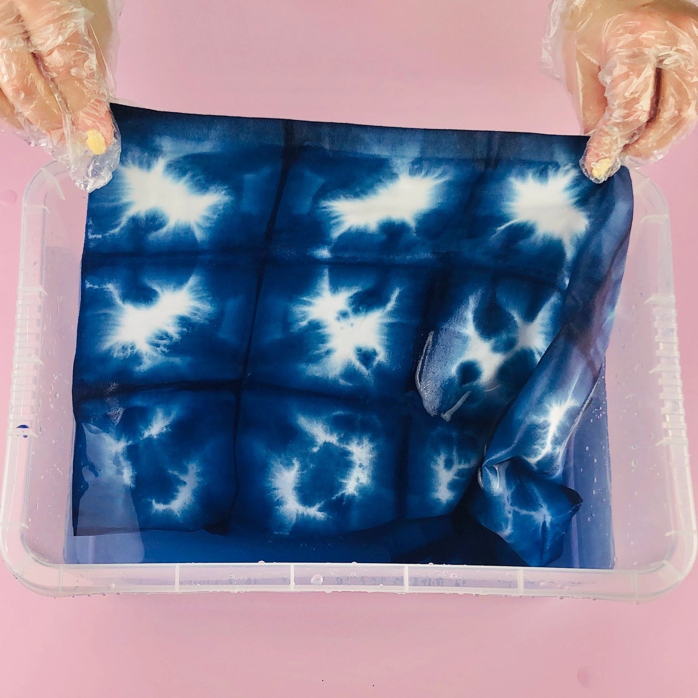 Person wearing plastic gloves demonstrating the rinsing  process during the making of a tie dye bag