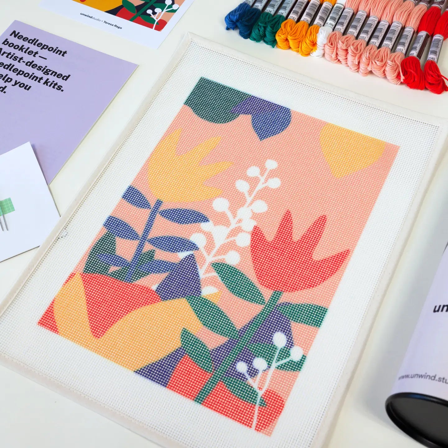 Close-up of some of the contents of a needlepoint kit with a vibrant tulip design, including a printed canvas and a variety of coloured threads