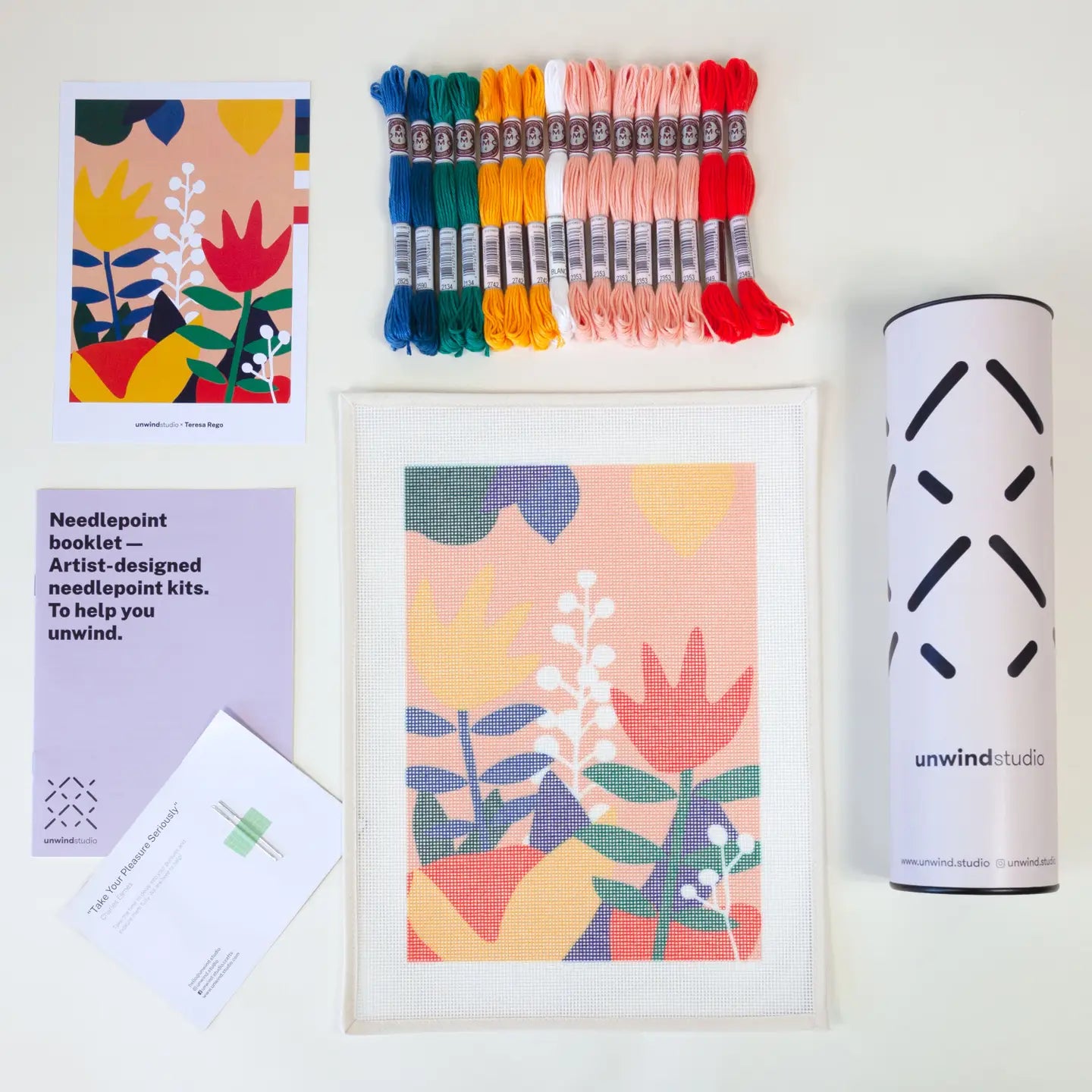 Contents of a needlepoint kit with an tulip-themed design, including a printed canvas, coloured threads, a photo of the original artwork, two tapestry needles, instruction booklet, and packaging tube
