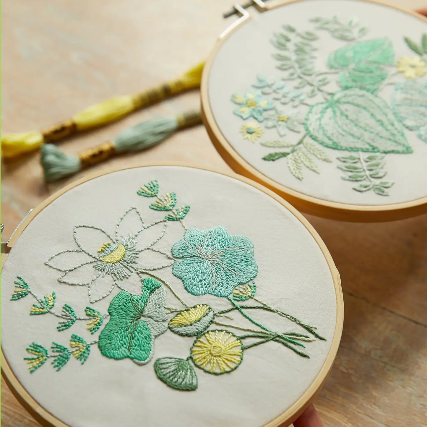 Two embroidery hoops with completed botanical designs on a wooden surface