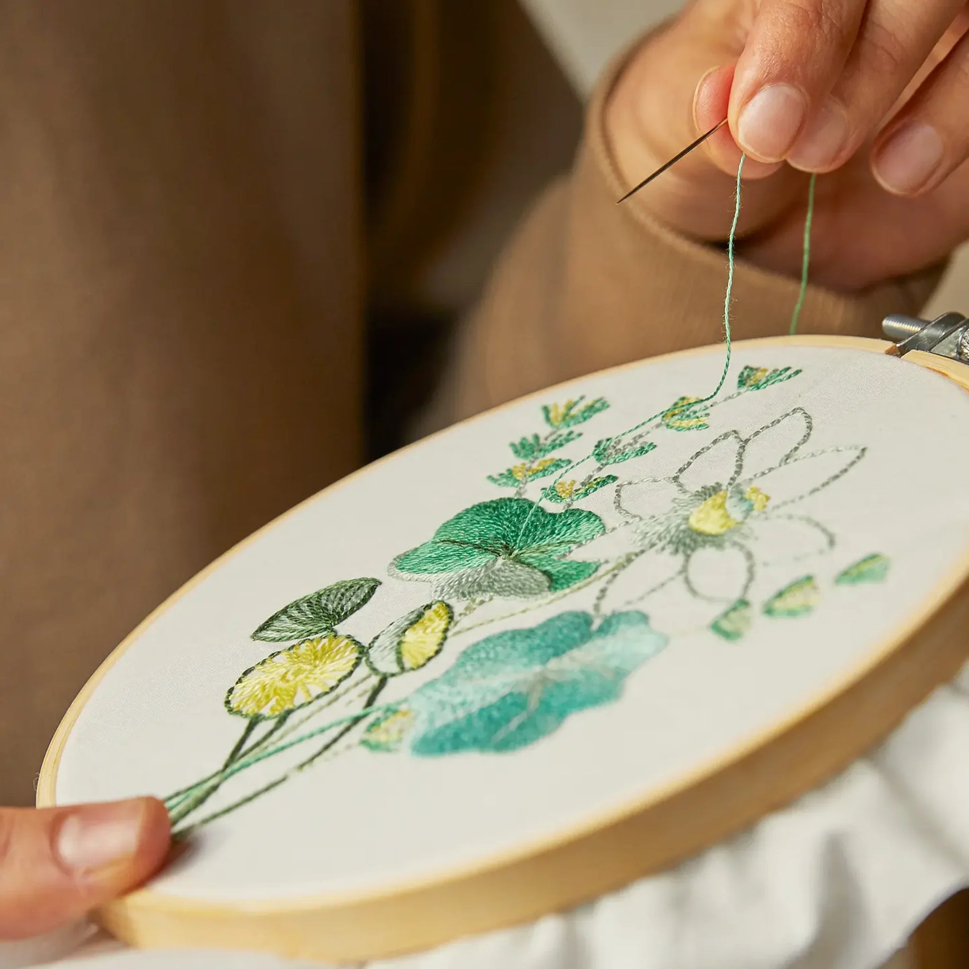 Person embroidering a botanical design on a hoop with green thread