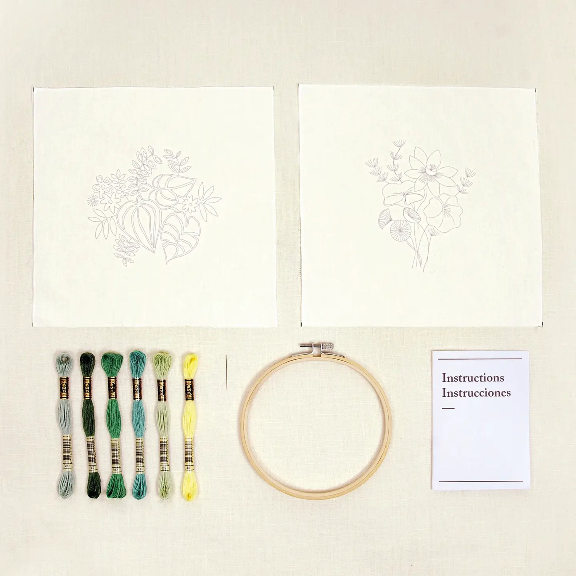 Botanical embroidery kit contents with patterns, threads, hoop, and instructions on a cream fabric background
